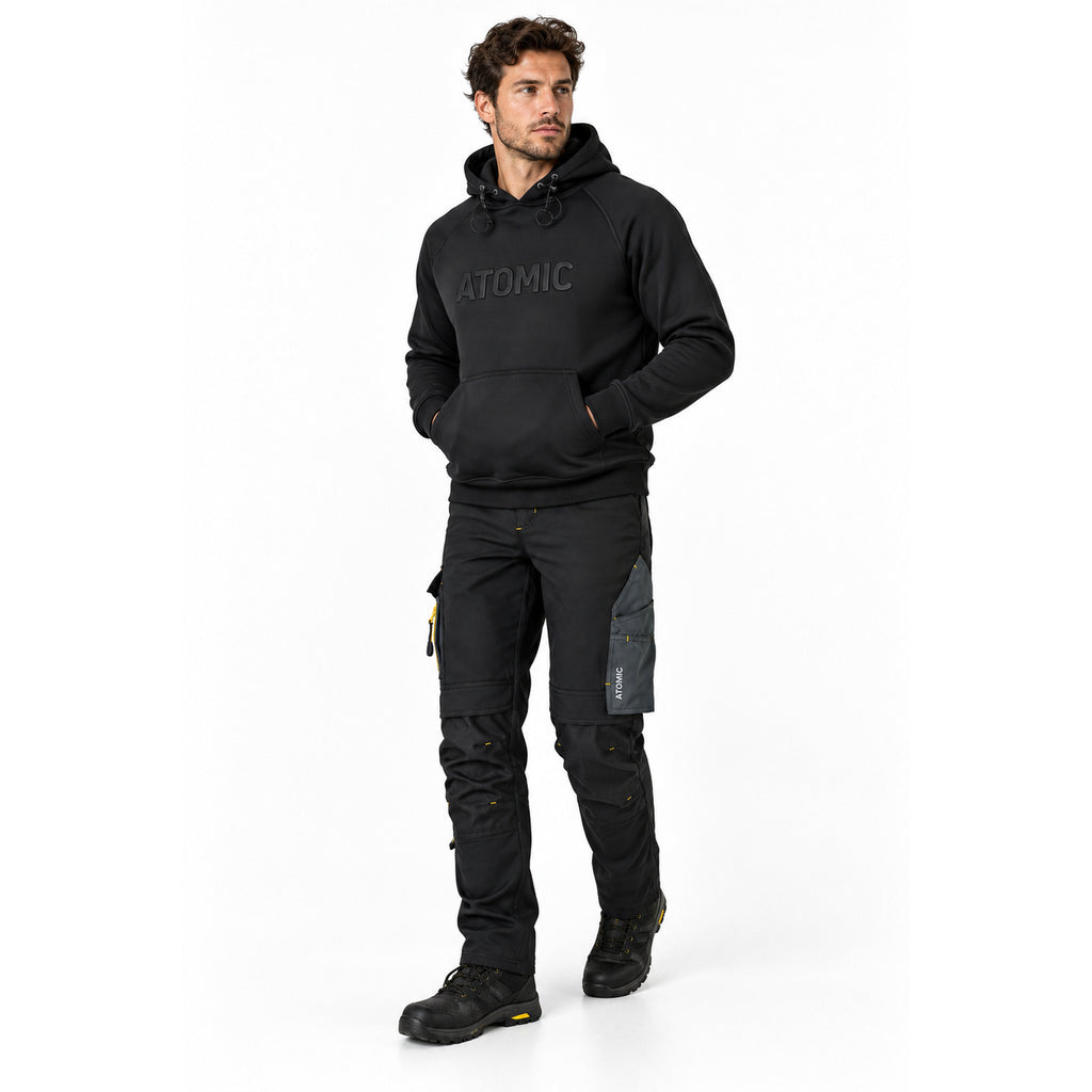 Male model wearing black ATOMIC technical work trousers and heavyweight logo hoodie with black work boots.