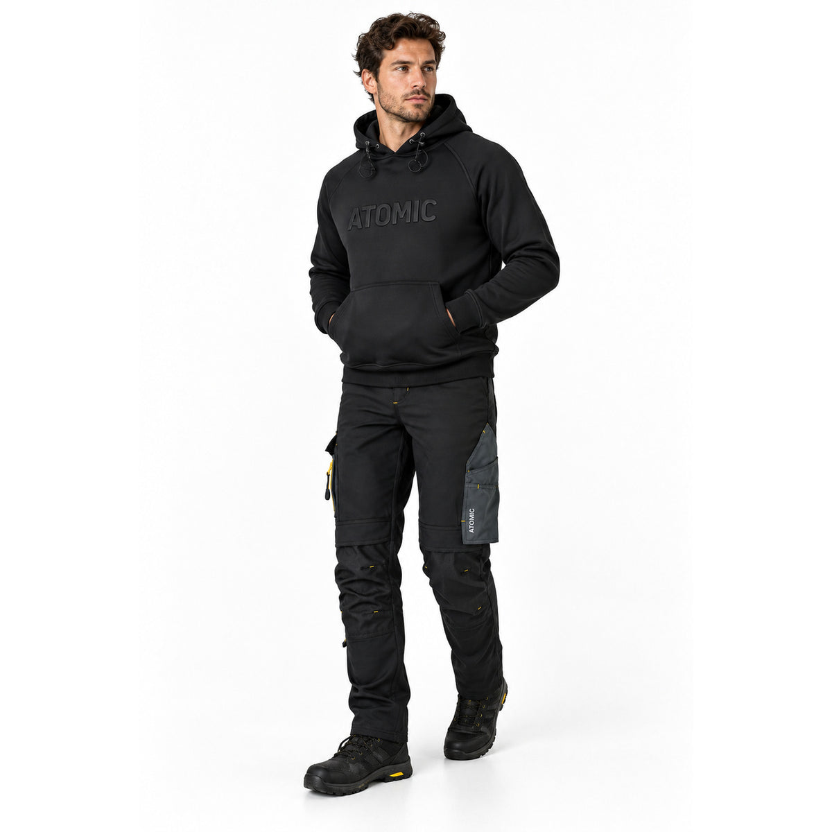 Male model wearing black ATOMIC technical work trousers and heavyweight logo hoodie with black work boots.