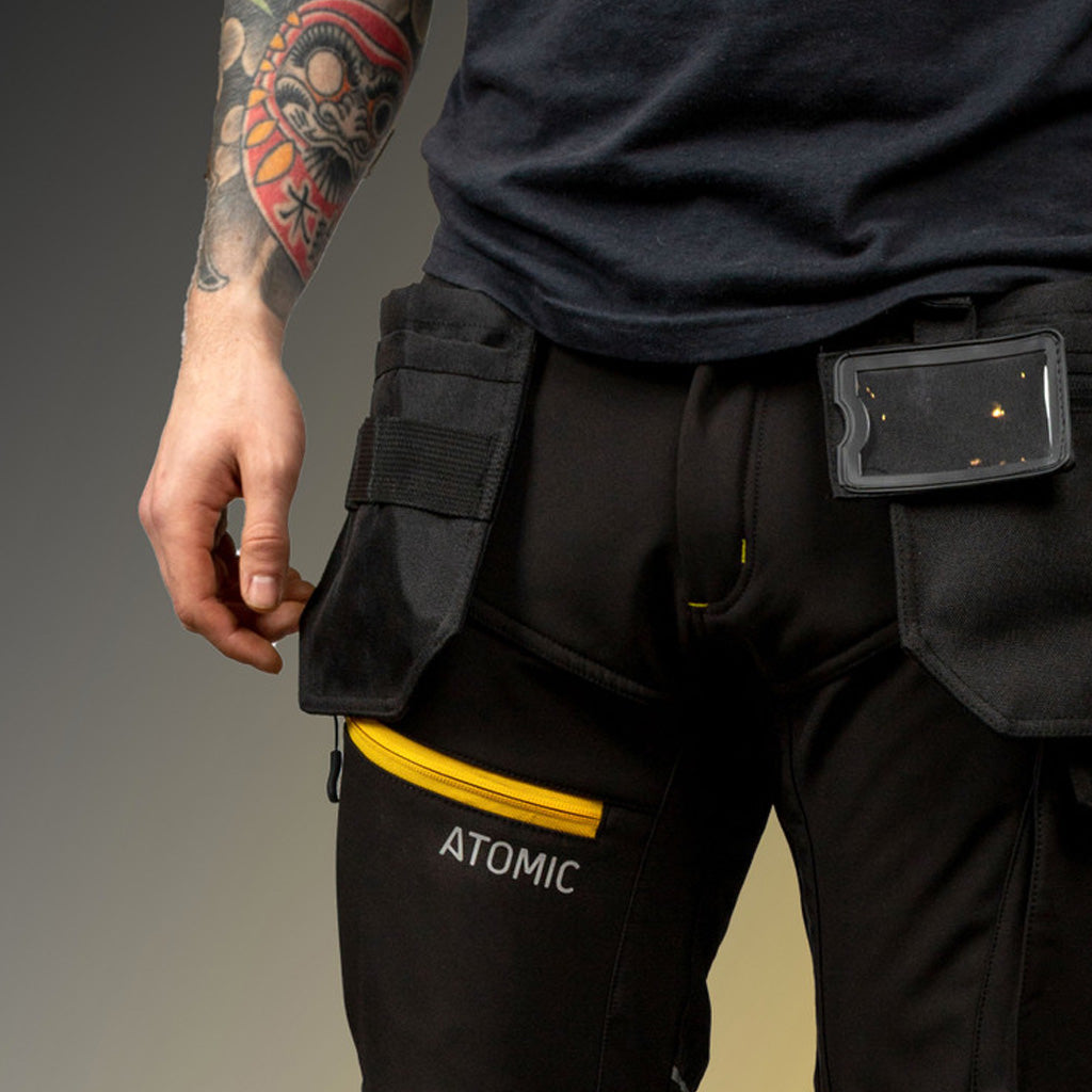 Person wearing black pants with a visible 'Atomic' brand label, on a gray background